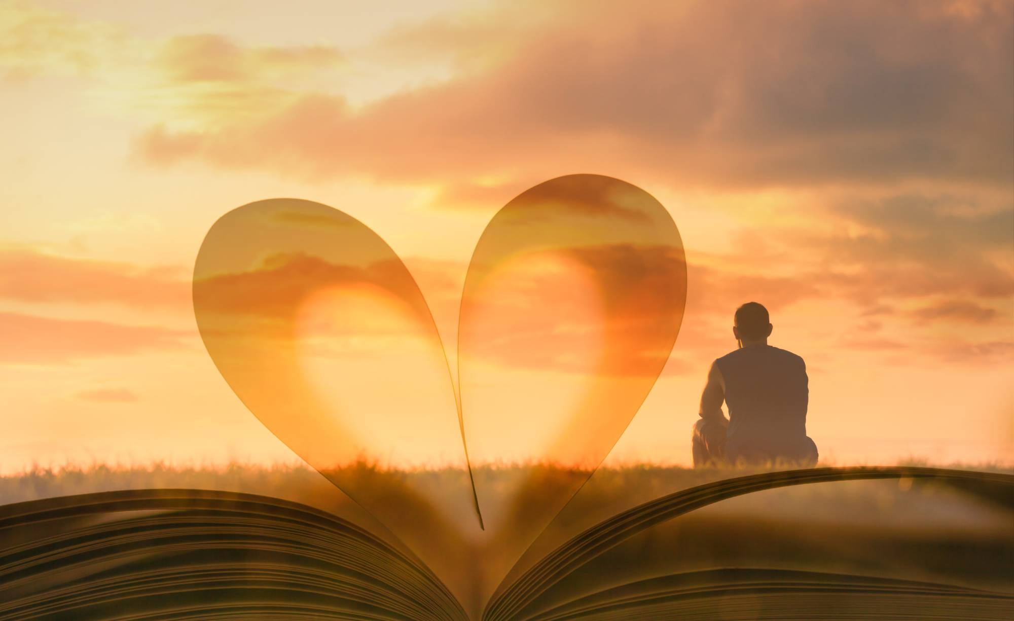 Man sitting on field looking at sunset with an overlayed book showing pages in the shape of a heart