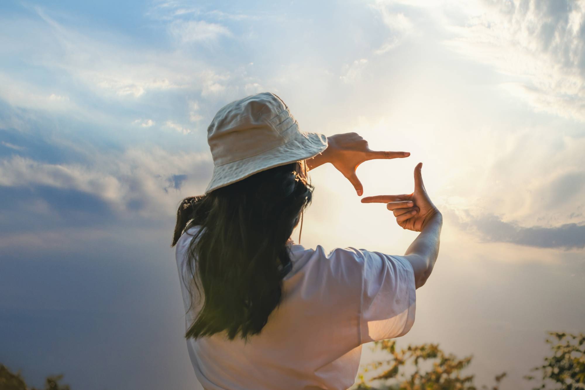 Woman looking through hands towards bright sky